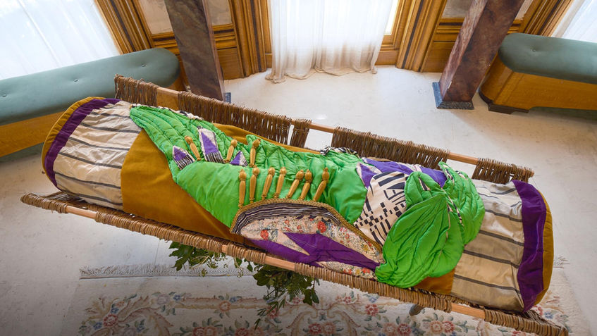 Green Wing burial shroud in vibrant green silk with patterned vintage silk panels and honey-coloured velvet, laid open to show its handcrafted design. Displayed in the Regency style show room.