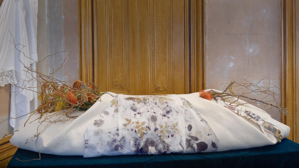 Angled view of a cream felt burial shroud with botanical print panel and flowers.