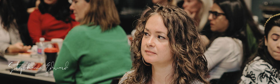 Stephanie Edward is a white woman with brown hair and brown eyes. She is sitting in the audience of a presentation, listening.