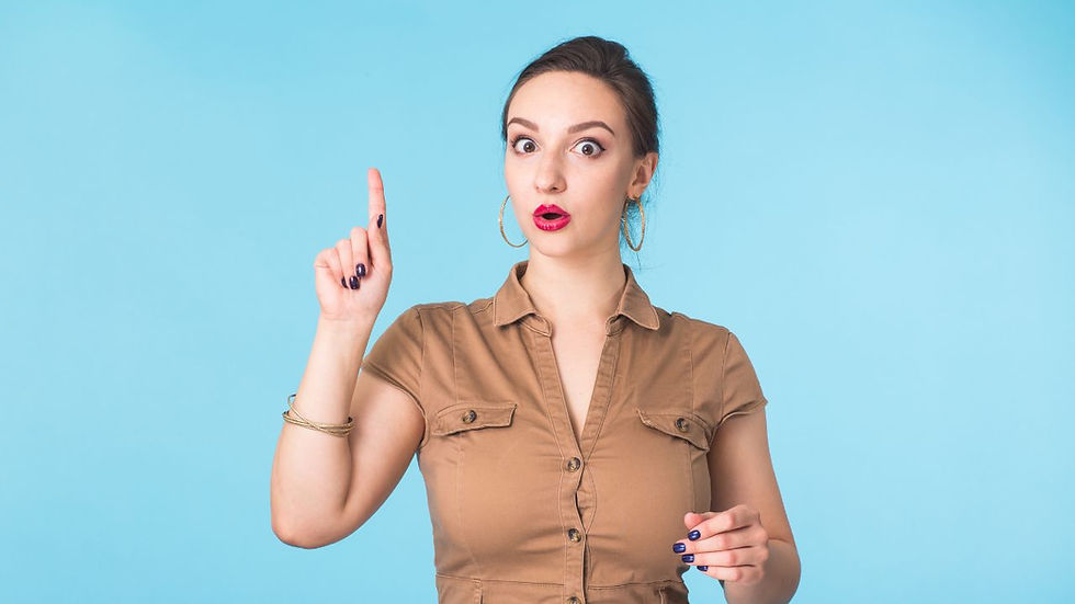 Woman in brown shirt raises index finger, looking surprised. Blue background, hoop earrings, bold lipstick, and expressive eyes.