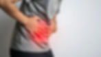 Person in gray shirt clutching stomach, standing against a white background. Red glow on abdomen suggests pain or discomfort.