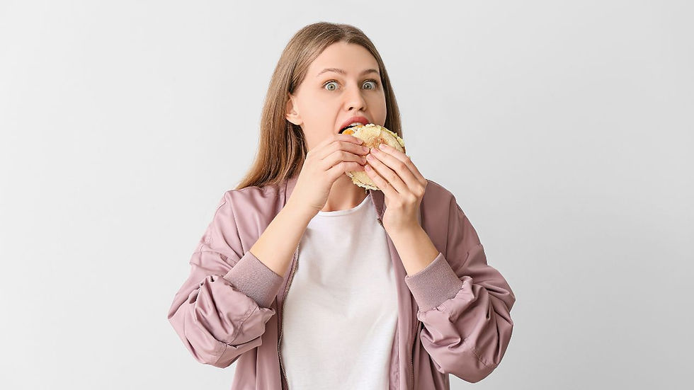 Woman in a pink jacket and white shirt eating a sandwich. She looks surprised. Plain light gray background.