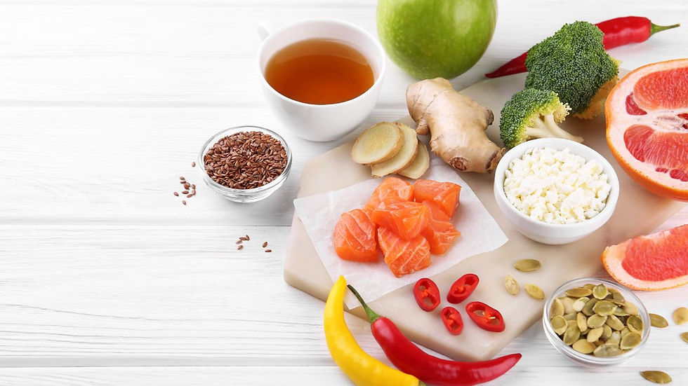 Fresh ingredients on a white table: salmon, ginger, grapefruit, broccoli, cheese, seeds, chili peppers, tea, and an apple. Bright and healthy.