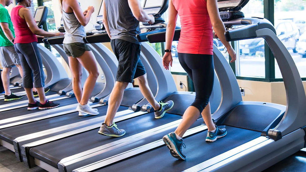 People exercising on treadmills in a gym, wearing colorful athletic clothing. Bright setting with large windows in the background.
