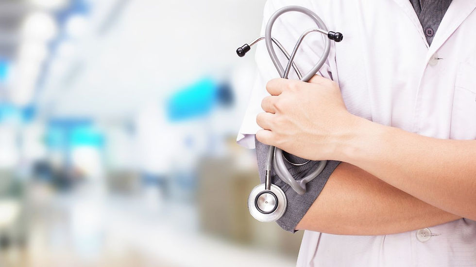Person in a white coat holds a stethoscope against a blurred hospital background, conveying professionalism and care.