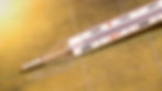 Glass thermometer showing 37°C rests on a warm-toned, textured surface. Red and black markings indicate temperature scale.