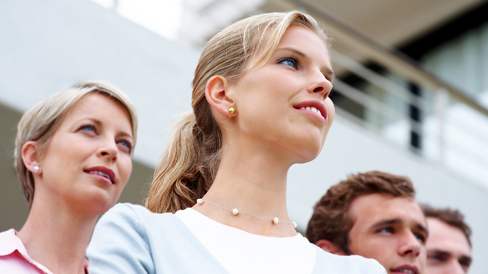 Close-up of four people looking upwards with hopeful expressions. Blurred modern building background. Soft lighting, light clothing.