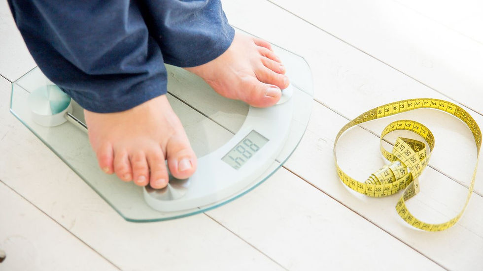 Feet on a glass scale reading 68.8. Yellow measuring tape coiled beside on white wooden floor. Casual atmosphere, navy clothing.