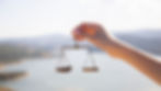 Hand holding a small balance scale against a blurred outdoor background. The mood is calm, with soft lighting and subtle colors.