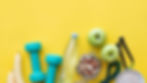Dumbbells, bananas, apples, nuts, a water bottle, jump rope, and oats on a bright yellow background, evoking a healthy lifestyle.