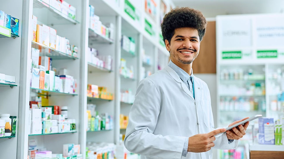 Smiling pharmacist in a white coat holding a tablet in a bright pharmacy. Shelves filled with colorful medicine boxes in the background.