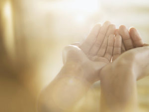 Hands open in prayer or supplication against a soft, golden bokeh background, conveying a sense of peace and hope.