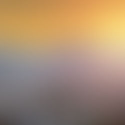 Cityscape at sunrise with snow-capped mountains in background. Buildings and houses fill the foreground, bathed in warm orange glow.