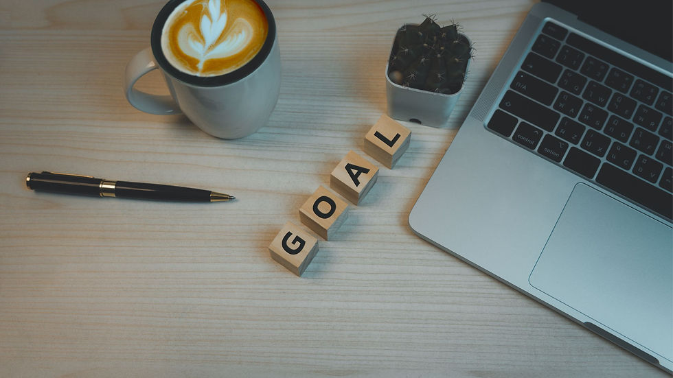 Laptop, coffee with latte art, pen, and blocks spelling "GOAL" on a wooden desk. Modern, organized workspace vibe.