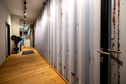 Moderner Flur mit rustikaler Containerwand im Industrial Design, hellem Echtholzboden, minimalistischer Deko und stilvoller Deckenspots-Beleuchtung – Bürogang mit urbanem Charakter.