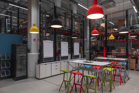 Moderner Workshop- und Meetingbereich in einer umgebauten Lagerhalle mit Tischen, bunten Stühlen und industrieller Beleuchtung