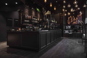 Modernes Café-Design von Influencerin Karo Kauer mit komplett schwarzer Inneneinrichtung, glänzenden schwarzen Wandfliesen, schwarzer Theke, stimmungsvoller Pendelleuchten und edlem Lounge-Bereich. Luxuriöses, trendiges Interior-Konzept mit starker Markenidentität und elegantem Industrial-Chic.