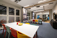 Moderner Besprechungs- und Aufenthaltsbereich mit bunten Stühlen, zwei großen Tischen, maritimen Raumtrennern und angrenzender Lounge – flexibler Meetingraum mit kreativer Wohlfühlatmosphäre
