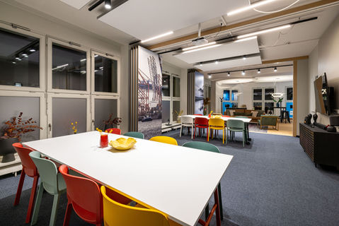 Moderner Besprechungs- und Aufenthaltsbereich mit bunten Stühlen, zwei großen Tischen, maritimen Raumtrennern und angrenzender Lounge – flexibler Meetingraum mit kreativer Wohlfühlatmosphäre