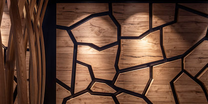 Detailaufnahme einer modernen Wandverkleidung in Holzoptik mit schwarzen, organisch verlaufenden Linien, die ein mosaikartiges Muster ergeben. Warmes Licht sorgt für stimmungsvolle Akzente. Ideal für Interior-Design, Lounge-Gestaltung oder moderne Gastronomie-Einrichtungen.