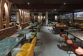 Stilvolles Café-Interieur mit grünen Marmor-Tischen, Lederbank, Designer-Stühlen in Gelb, Grün und Rostrot, organischen Holzelementen, eleganter Beleuchtung und modernem Boutique-Design.

