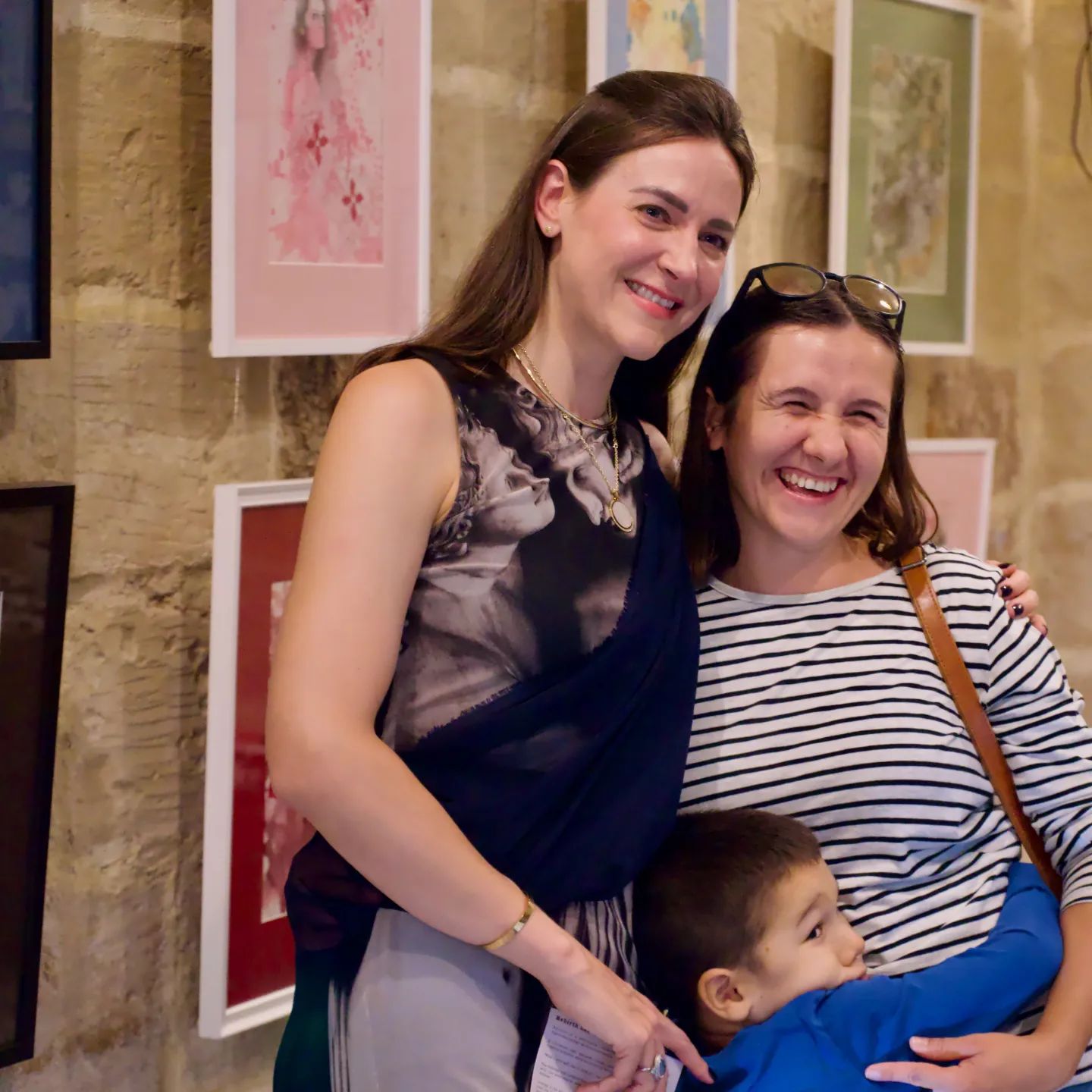 Artist taking a photo with a mother and son in front of the original artworks in a collective exhibition