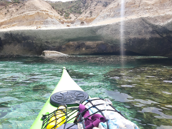 Sea kayak approaching a secluded sea arch in crystal clear waters off Malta