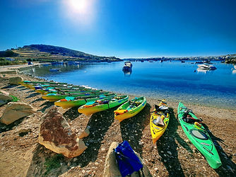 Rainbow Orca sea kayak fleet at Mistra Bay Malta ready for a guided kayaking tour on calm Mediterranean waters.