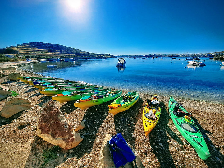 Rainbow Orca sea kayak fleet at Mistra Bay Malta ready for a guided kayaking tour on calm Mediterranean waters.