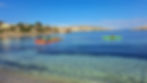 People kayaking in colorful kayaks on clear blue sea near a rocky coastline at Santa Marija Beach, Kemmuna (Comino); bright sunny day with blue sky.
