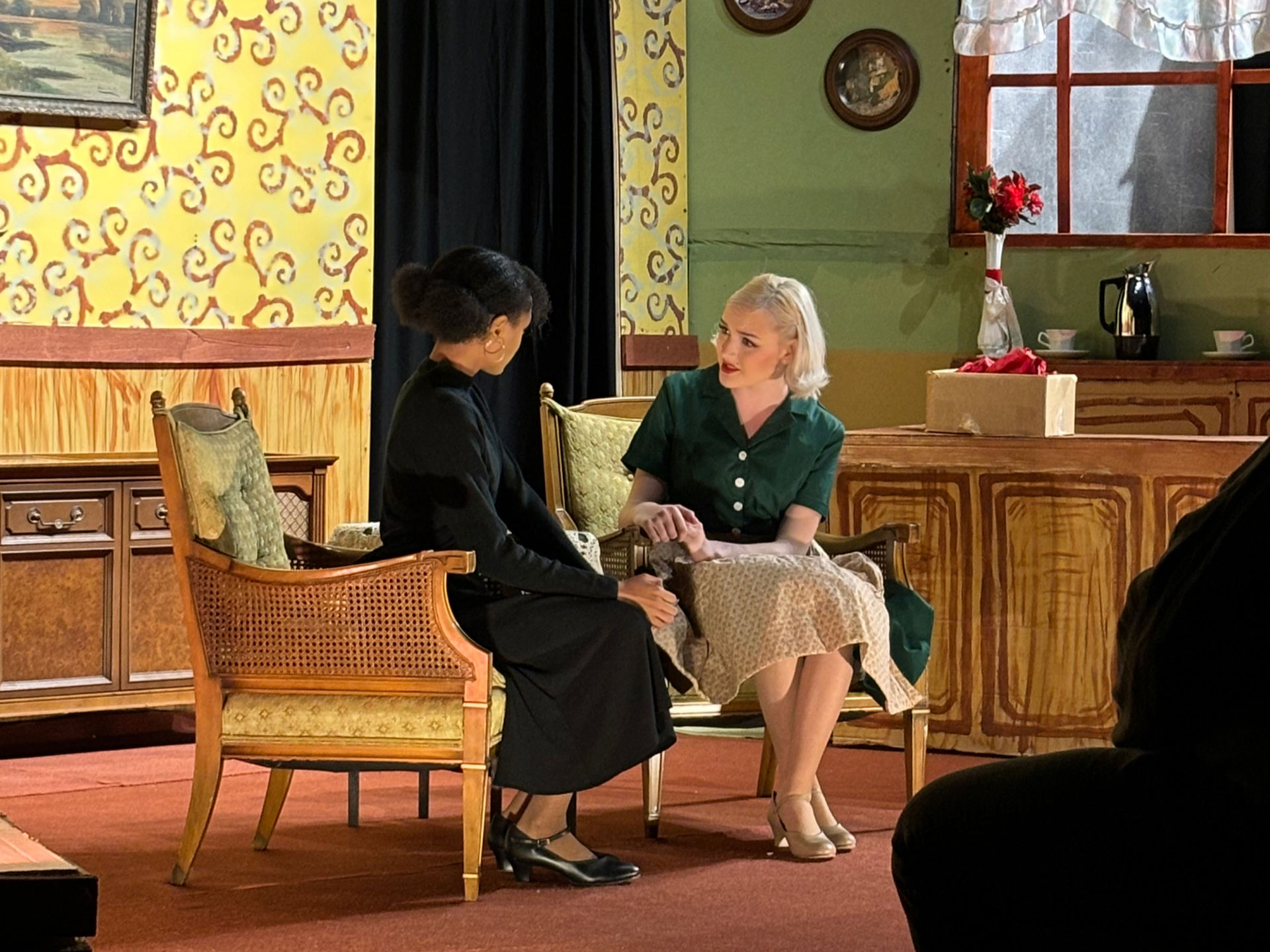 Two Kairos students perform on stage, the set is decorated to resemble a 1940s living room.