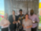 A diverse group of Kairos supporters hold their campion awards in front of a glittering backdrop.