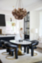 Elegant kitchen with dark leather chairs around a marble table, brown chandelier above. Person opens a black cabinet. Bright and modern decor.