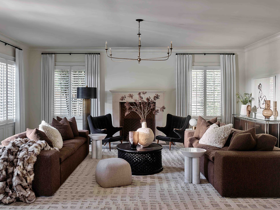 Stylish, symmetrical living room with brown sofas, black chairs, fireplace, chandelier, and white shutters in a calm neutral palette.
