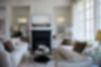 Modern living room with cream sofas, black fireplace, patterned lampshade, and wall art. Large windows; cozy and bright atmosphere.