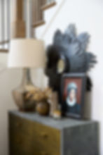 Dresser with a table lamp, dried flowers, a painted portrait in a wooden frame, and a decorative mirror in a modern staircase setting.