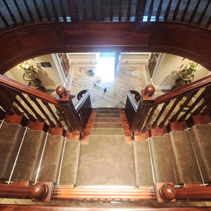 A grand staircase with brown carpet installed as a runner