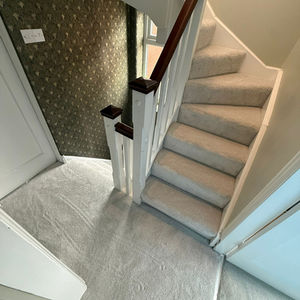 Carpeted staircase with patterned wallpaper and white railings.
