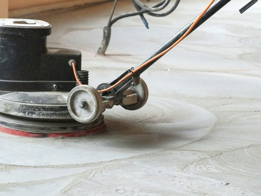 A floor sanding machine is being used to remove layers of old adhesive