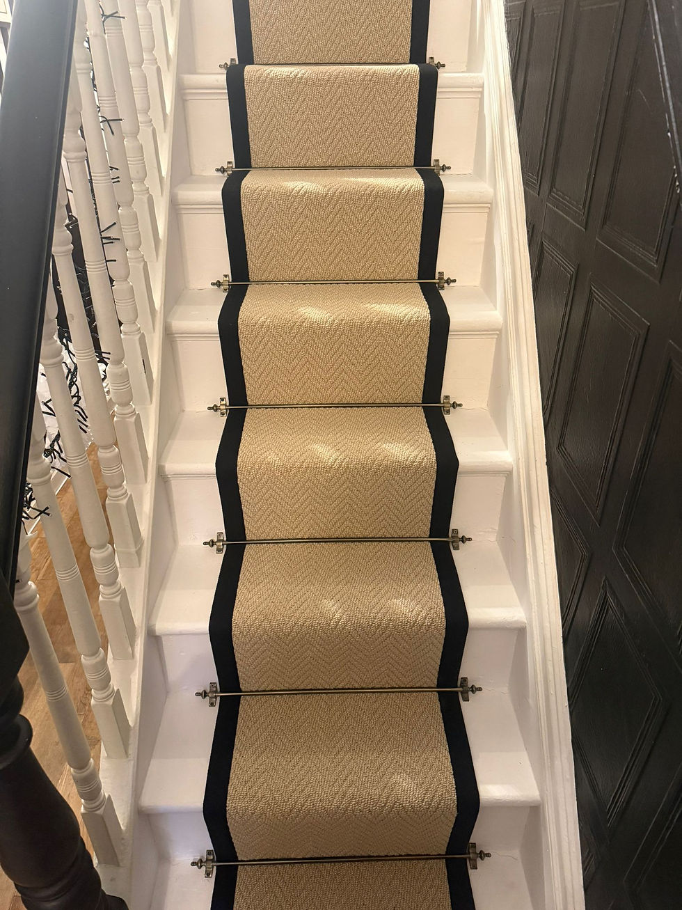 Caramel Herringbone stair runner with contrasting black taped edges and stair rods on wooden stairs