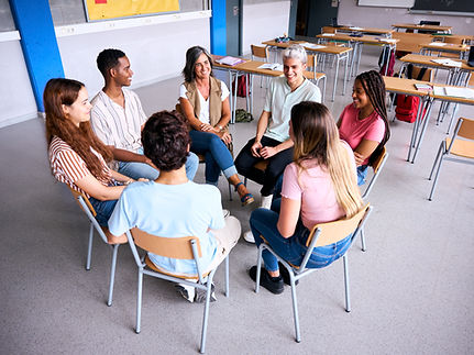 A group of students and a teacher sit in a circle during a school group therapy session, p