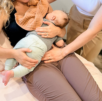 Miki Eaton providing postpartum recovery support for a mother with her baby resting on her lap.
