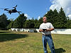 a man standing outdoors in a sunlit open space, holding a drone controller_