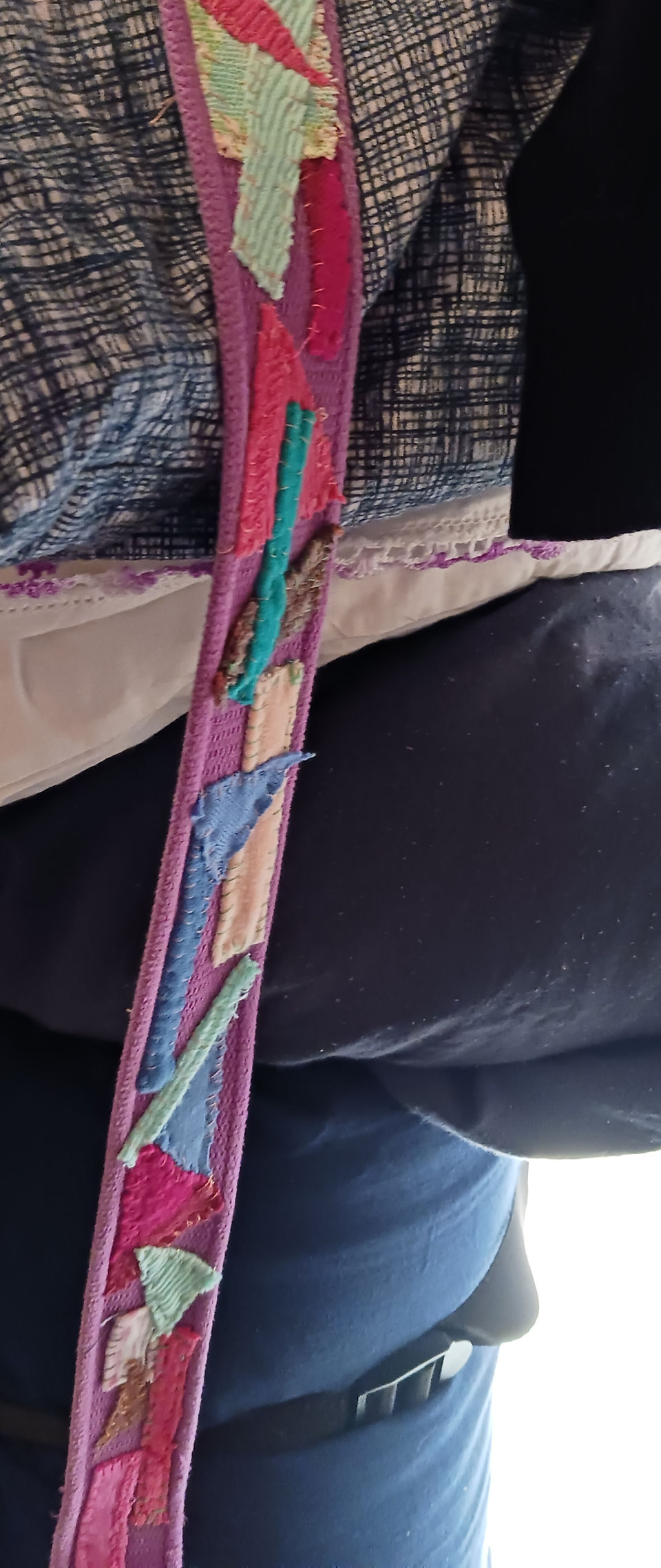 A purple canvas belt decorated with small pieces of colorful cloth that have been seen on by hand.  An example of my upcyclng work.