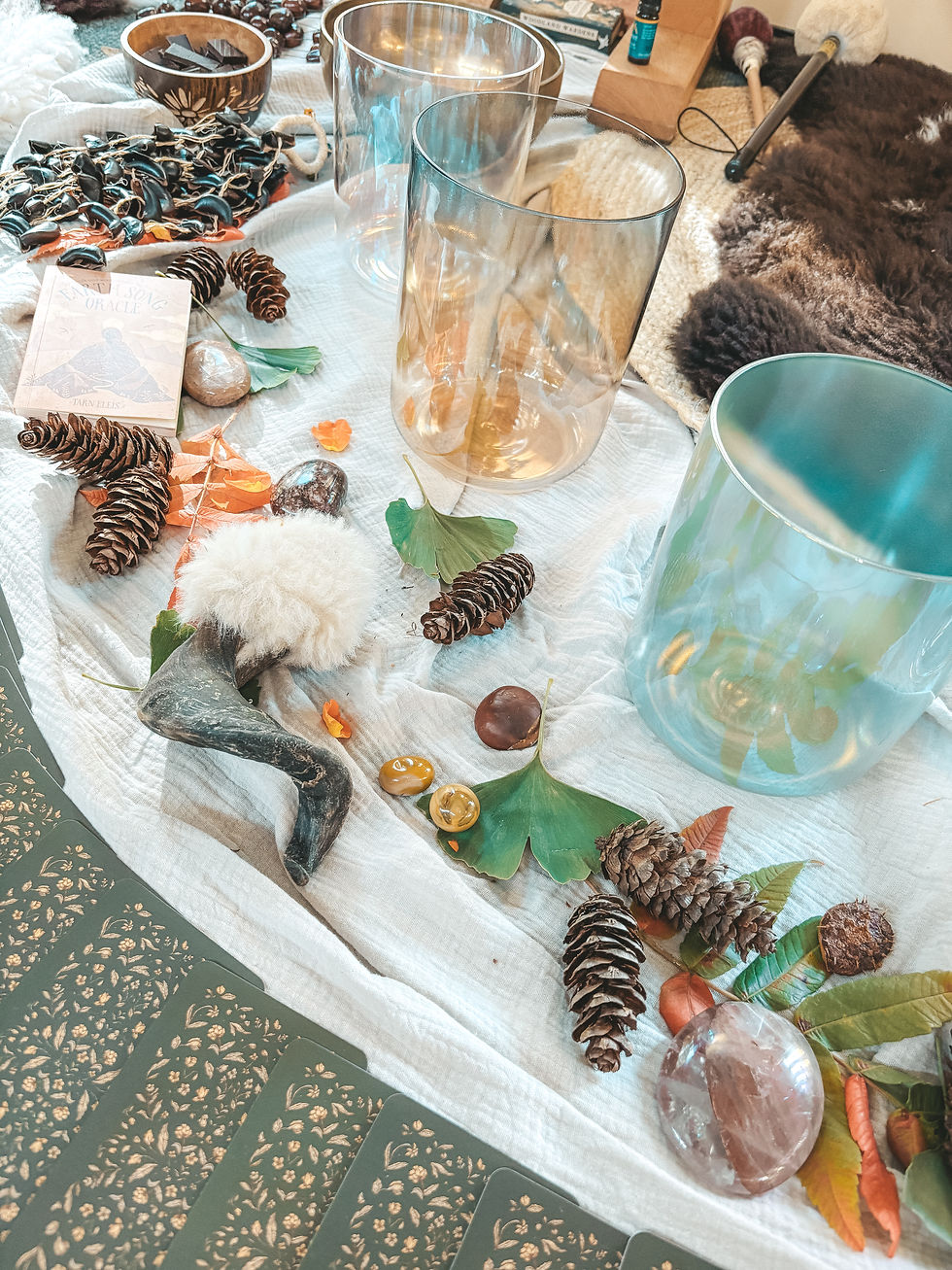 Boho flat lay of glass bowls, crystals, a Rebecca Campbell book, and leafy garland on linen beside a fur rug.