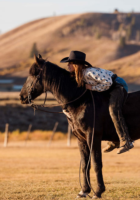 Girl on a horse leaning in close to its neck while looking toward the distant scenery