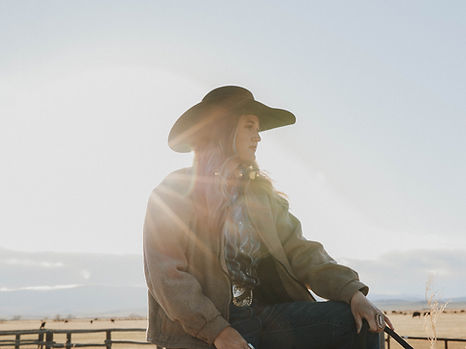 Girl sitting on a wooden fence with Wyoming mountains at sunset