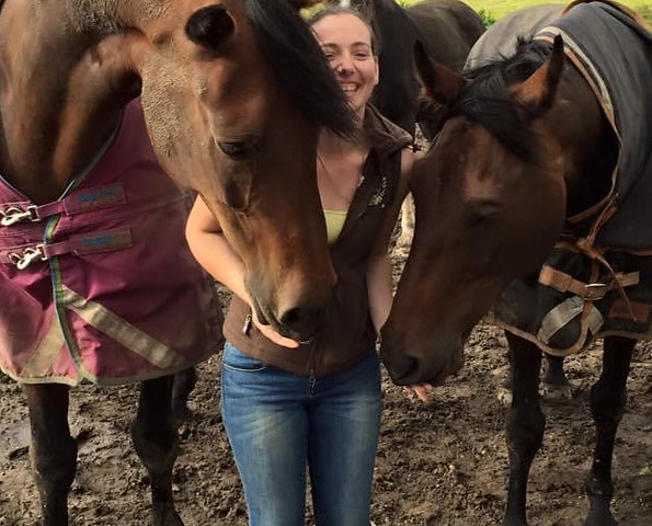 Girl with 2 horses in a field, the horses are wrapping their heads around her.