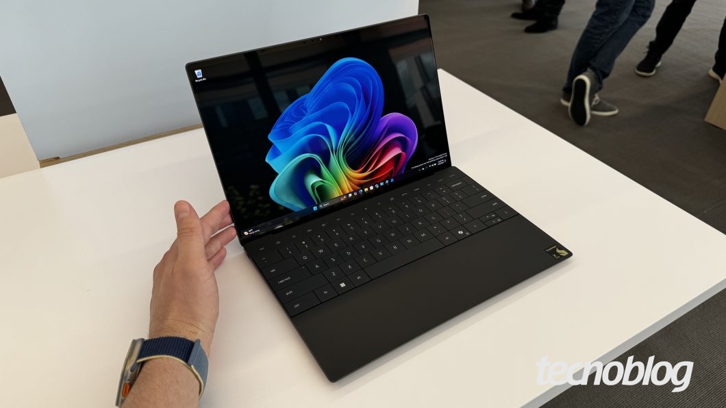 Fotografia mostra um notebook Dell XPS 13 de cor preta, com chip Snapdragon, sobre uma mesa branca. Na parte inferior direita, a marca d'água do "tecnoblog" é visível.