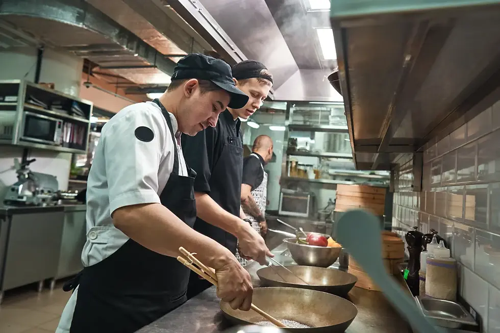 Cocina profesional con chefs cocinando en línea usando woks y utensilios tradicionales en ambiente moderno